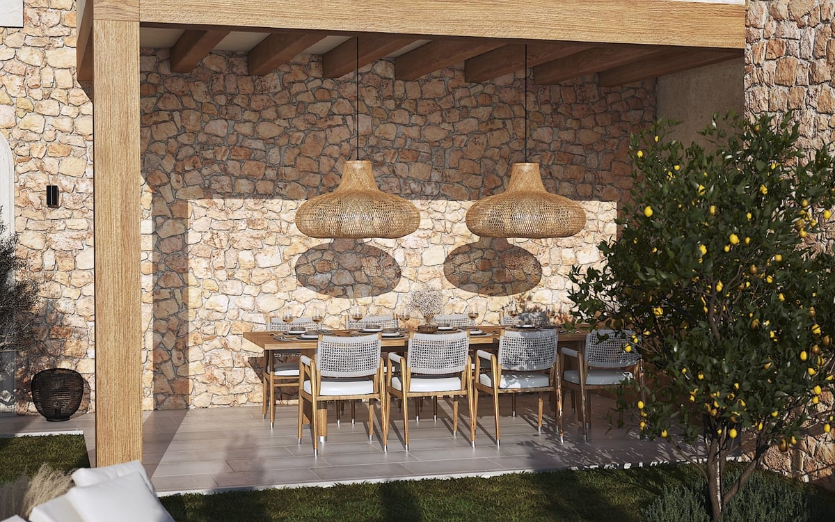 Comedor exterior cubierto con mesa de madera, lámparas de mimbre y pared de piedra natural rústica.