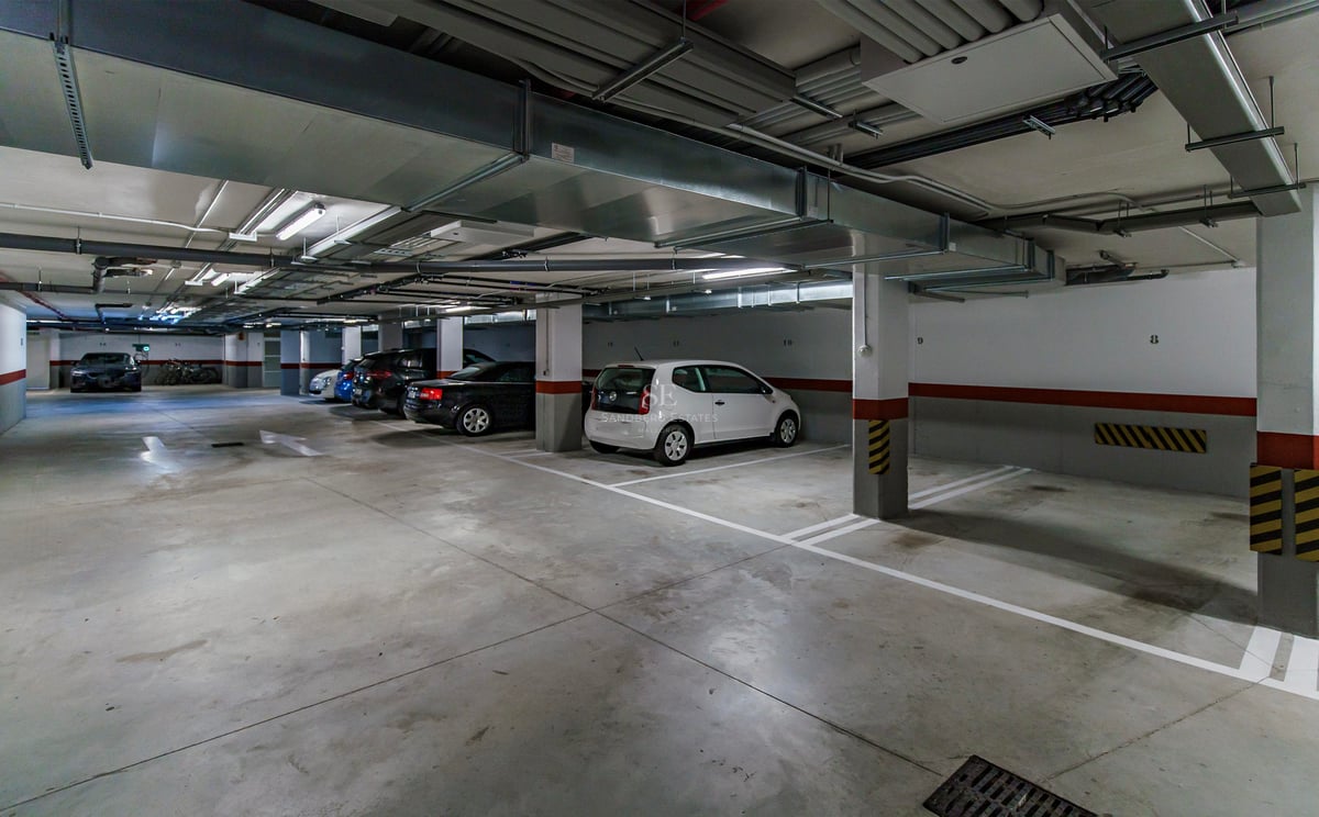 Parking souterrain éclairé avec places numérotées et voitures garées sous des conduits de ventilation.