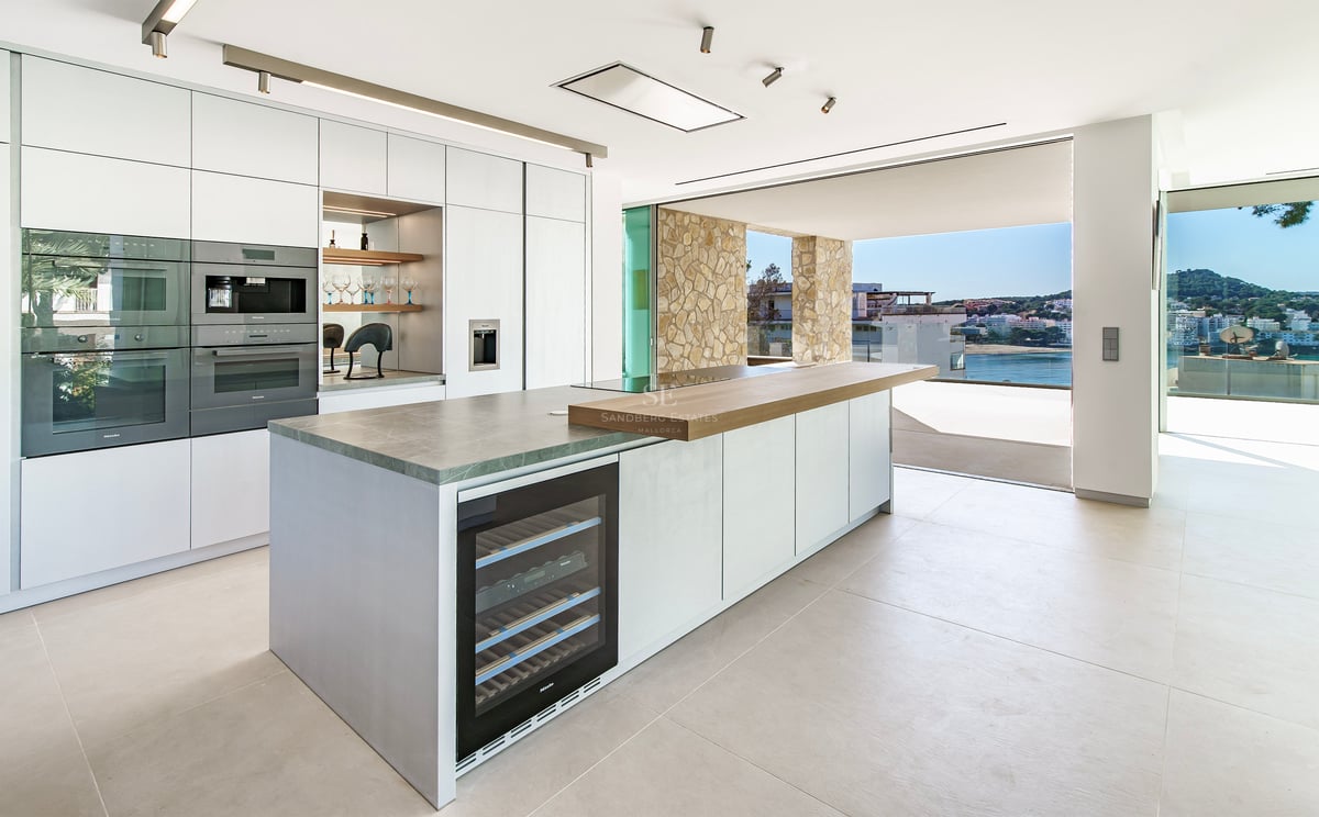 Cuisine minimaliste moderne avec îlot central, cave à vin et baies vitrées ouvrant sur une terrasse vue mer.