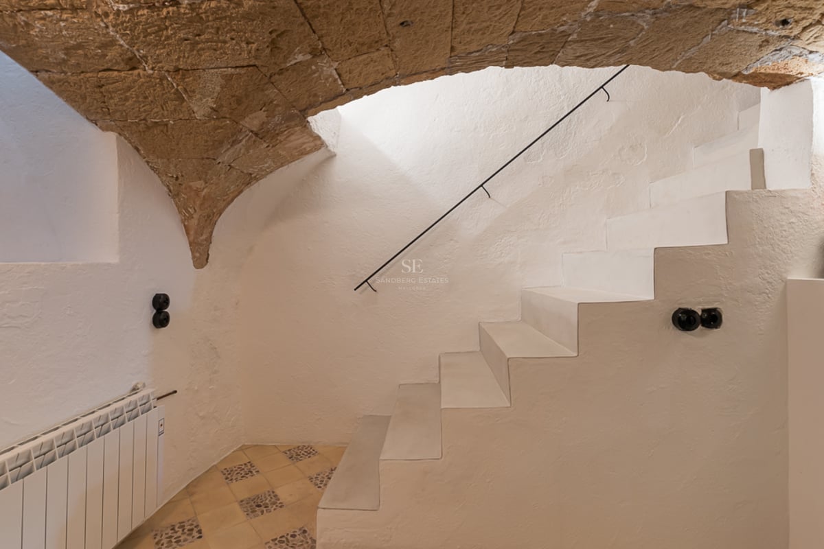 Minimalist white staircase under a natural stone arch in a renovated Mallorcan townhouse.