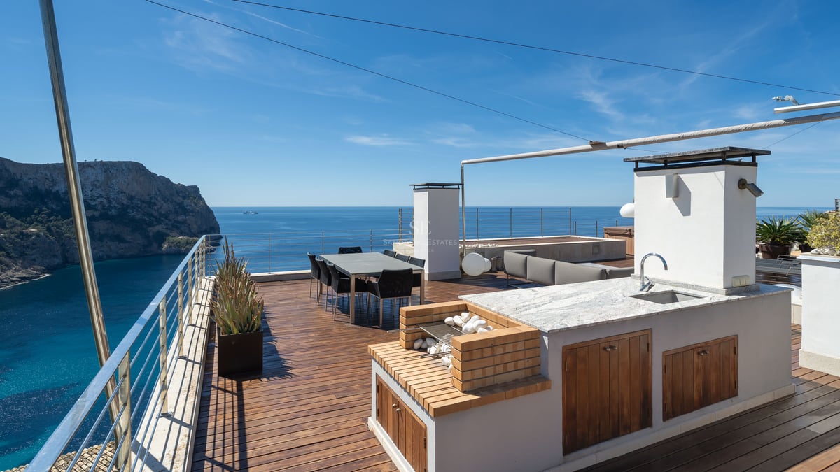 Terrasse de luxe sur le toit avec cuisine extérieure, coin repas et vue panoramique sur une baie méditerranéenne.