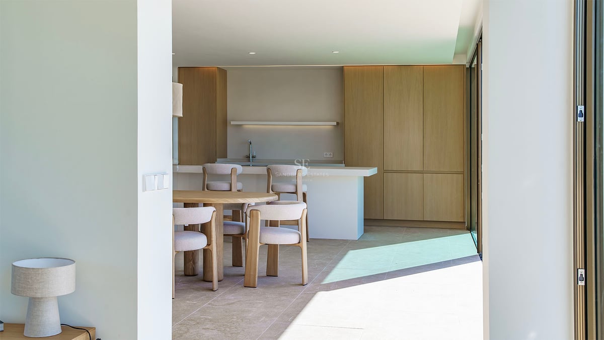Cuisine moderne lumineuse avec placards en chêne clair, îlot en pierre blanche et table à manger circulaire en bois.