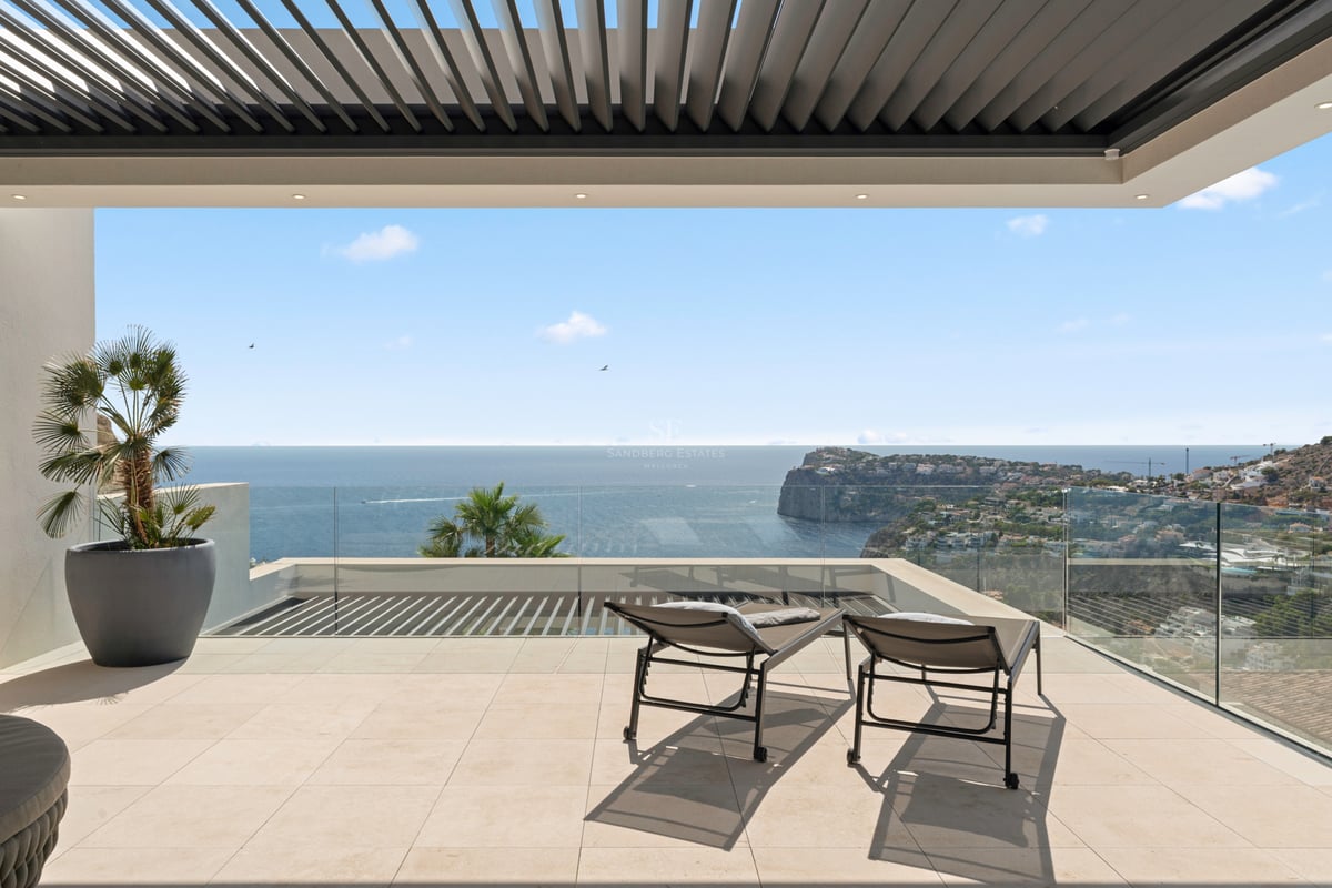 Terrasse moderne avec garde-corps en verre, deux chaises longues et vue imprenable sur l'océan et les falaises.