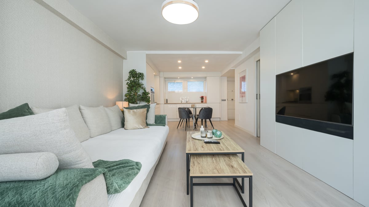 Salon lumineux avec canapé blanc, parquet clair et grand téléviseur intégré dans un meuble mural blanc.