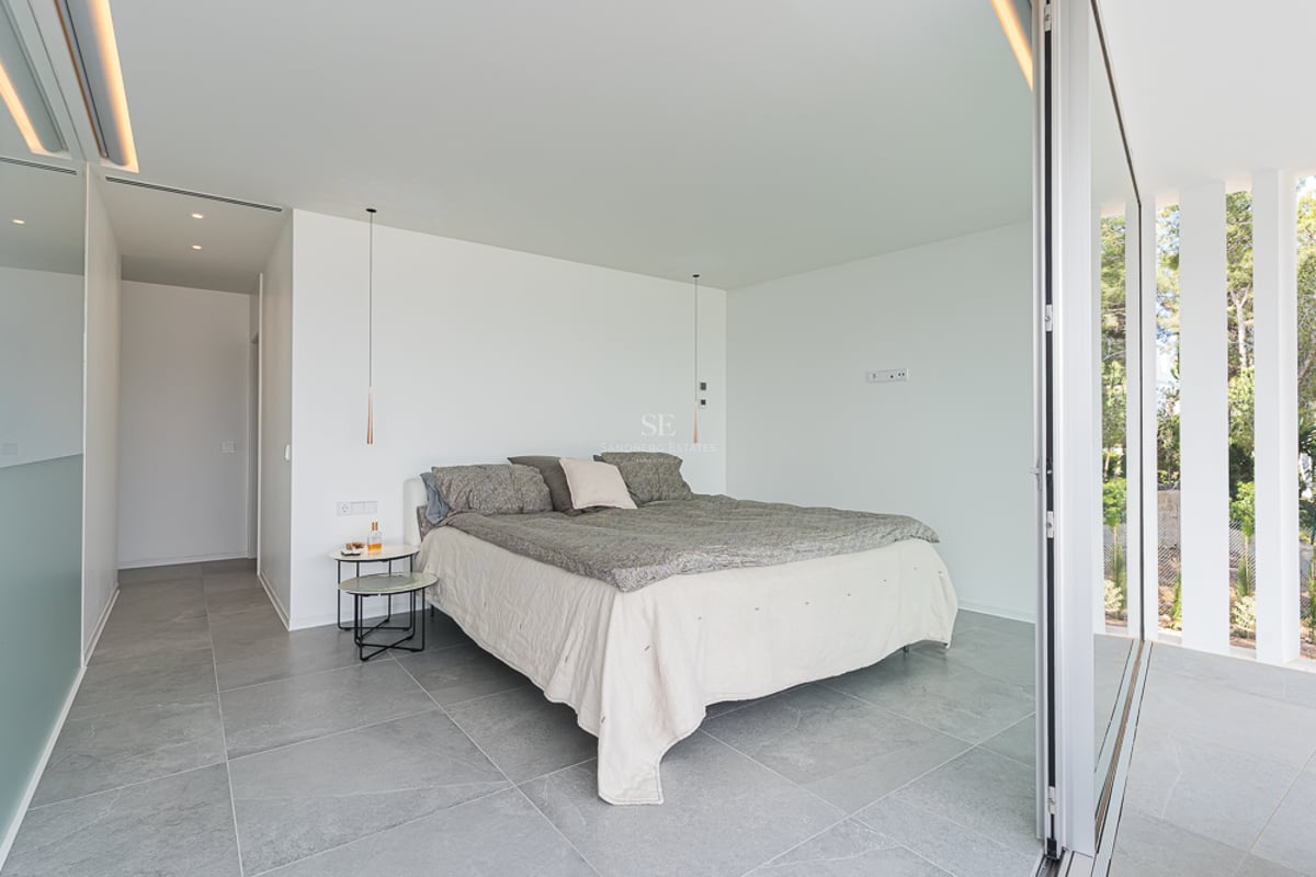 Chambre minimaliste avec sol en pierre grise, murs blancs et grande baie vitrée coulissante donnant sur le jardin.