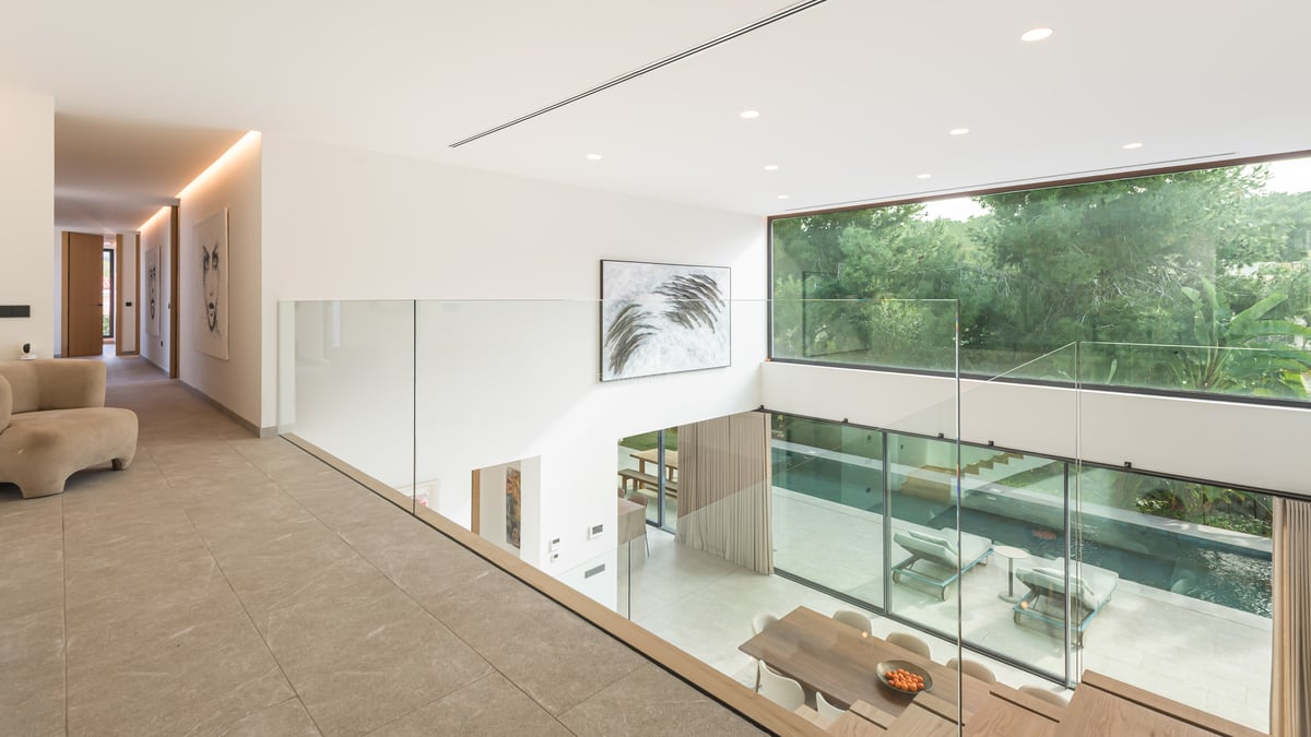 Vue depuis une mezzanine en verre sur un salon à double hauteur avec de grandes baies vitrées donnant sur la piscine.