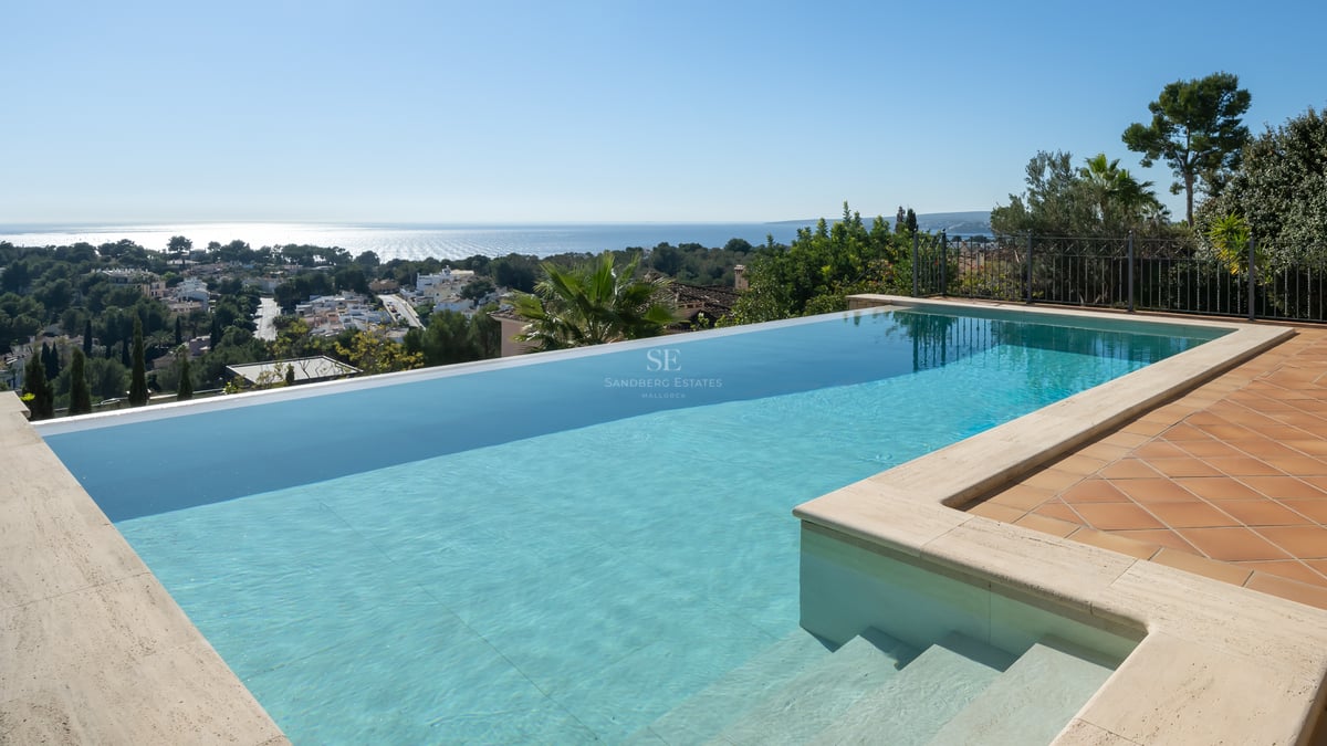 Piscine à débordement en L avec margelles en travertin et terrasse en terre cuite dominant le littoral et la mer.