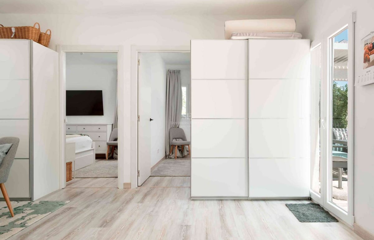 Couloir intérieur lumineux avec de grands placards blancs coulissants et un sol en bois clair menant à une chambre.