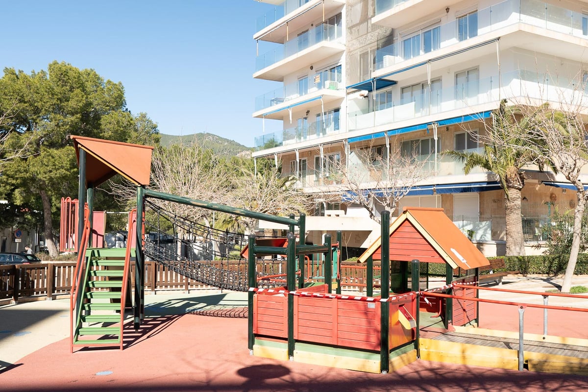 Aire de jeux pour enfants avec structures en bois et sol sécurisé devant un immeuble moderne.