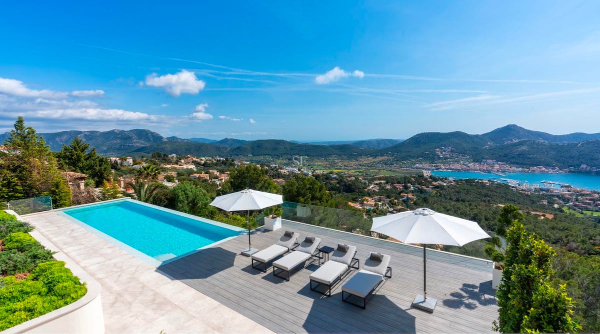 Terrasse extérieure avec piscine bleue, bains de soleil modernes, parasols blancs et vue sur les montagnes et la mer.