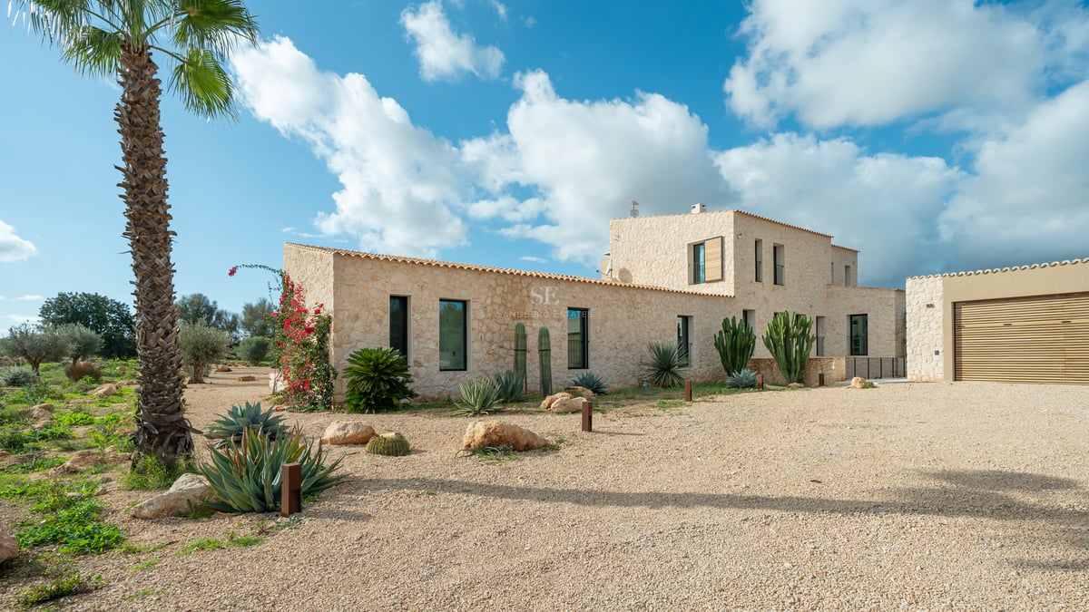Façade en pierre naturelle d'une villa moderne avec jardin de cactus et allée en gravier sous un ciel bleu.