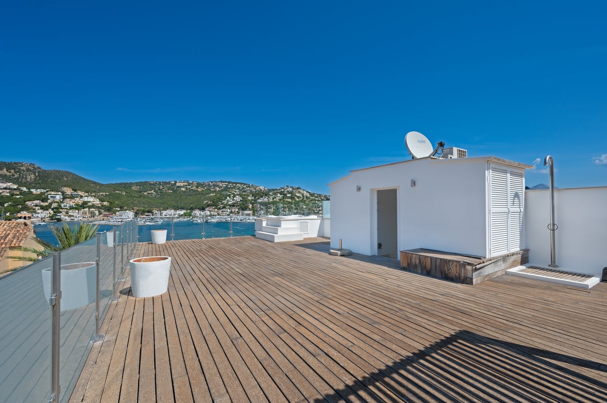 Grande terrasse de toit en bois avec garde-corps en verre offrant une vue sur une marina méditerranéenne.