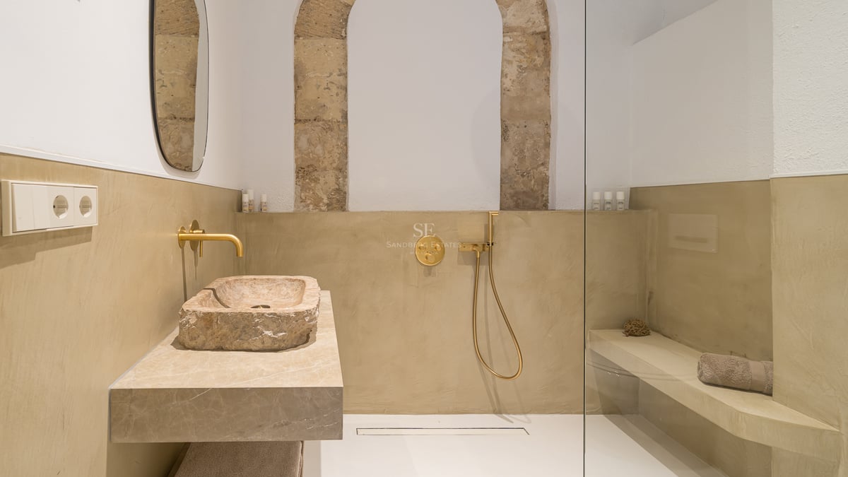 Salle de bain moderne avec vasque en pierre brute, robinetterie dorée et douche à l'italienne avec arche en pierre.