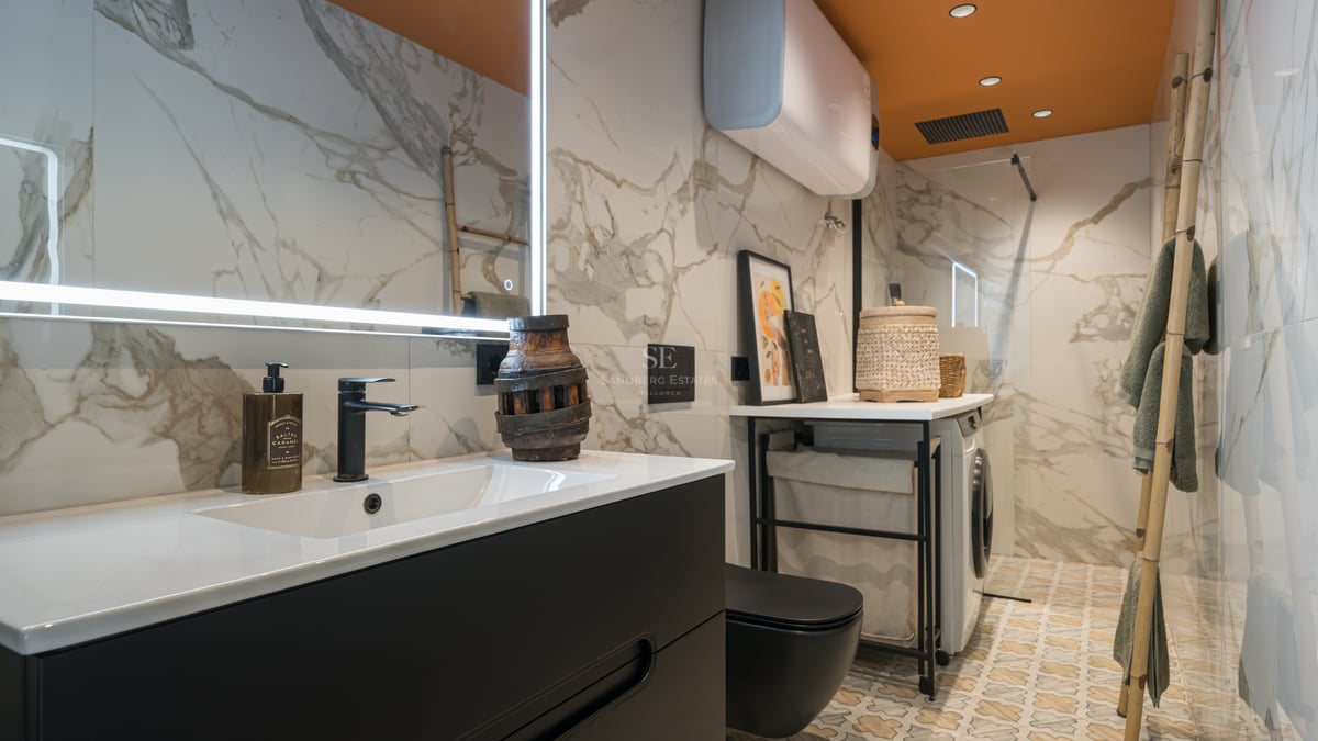 Salle de bain moderne avec murs en marbre, meuble noir mat, sol à motifs et coin buanderie intégré.