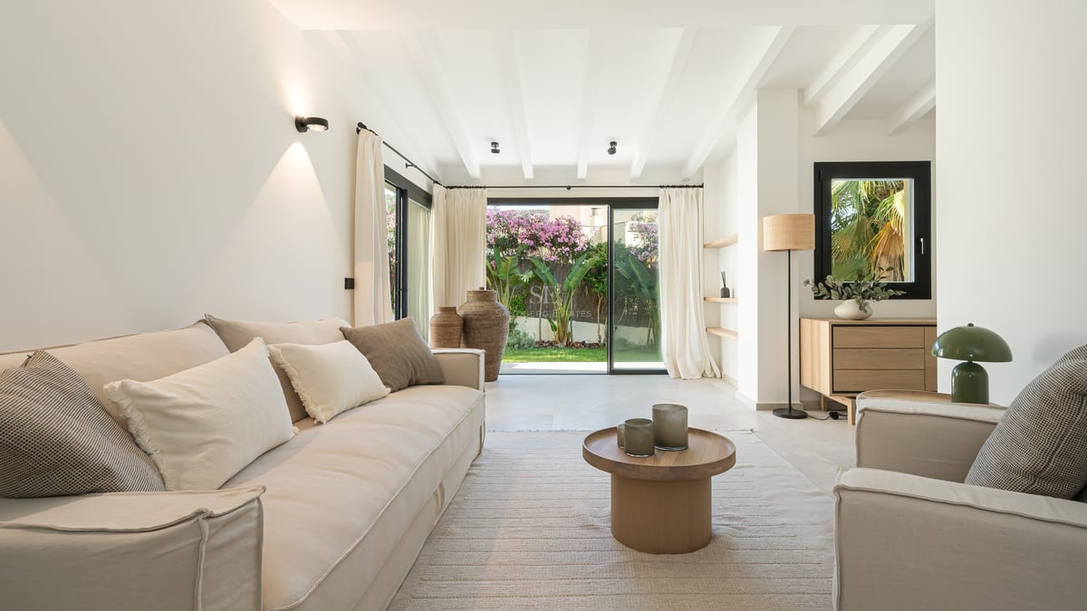 Salon lumineux avec canapés beiges et grandes baies vitrées ouvrant sur un jardin privé.