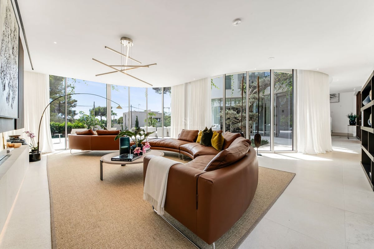 Salon moderne lumineux avec canapé en cuir cognac courbé et grandes baies vitrées donnant sur un jardin privé.