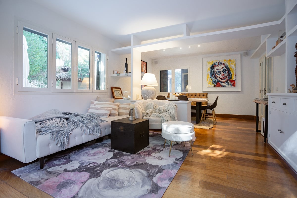 Salon à aire ouverte avec canapés blancs, tapis floral, parquet en bois et coin repas en arrière-plan.