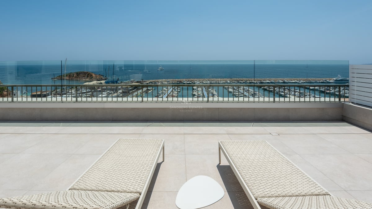 Deux bains de soleil sur une terrasse en pierre surplombant un port de plaisance et la mer Méditerranée.