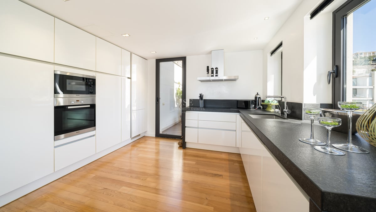 Cuisine moderne blanche avec plans de travail en pierre sombre, parquet en chêne, appareils intégrés et accès terrasse.