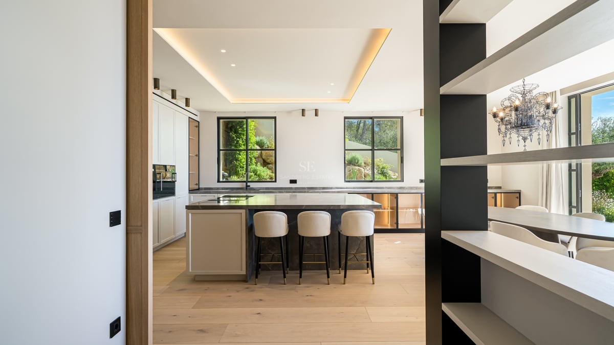 Cuisine moderne à plan ouvert avec un îlot en marbre sombre, parquet en chêne clair et fenêtres sur le jardin.