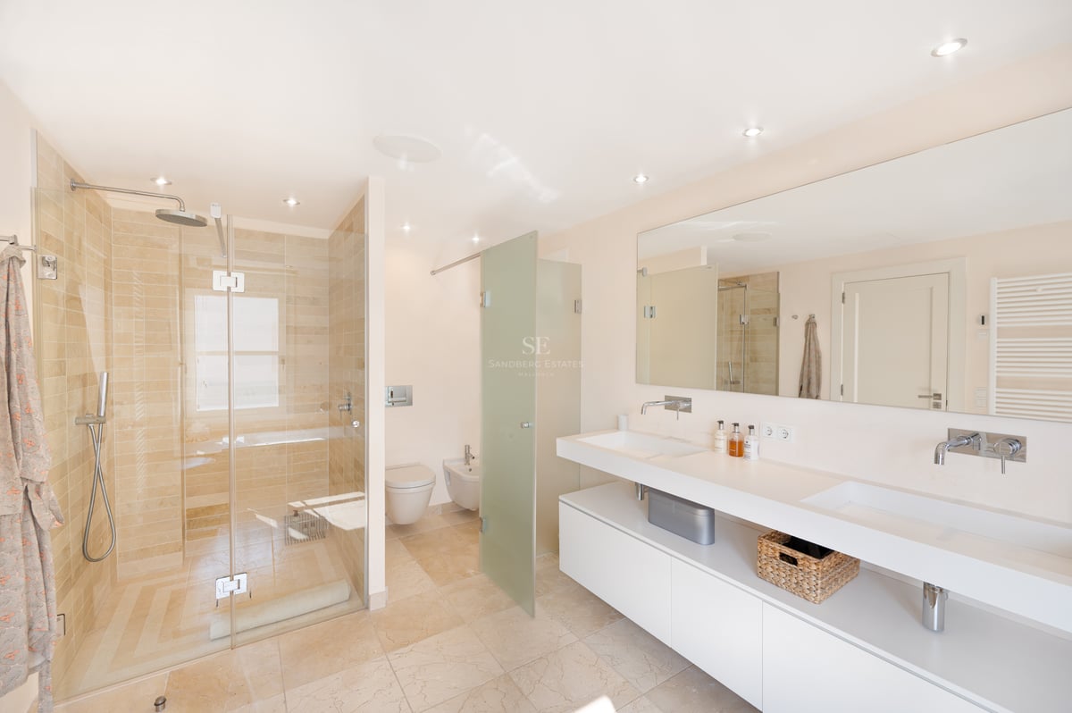 Salle de bain lumineuse avec double vasque blanche, grand miroir et douche à l'italienne en pierre naturelle beige.