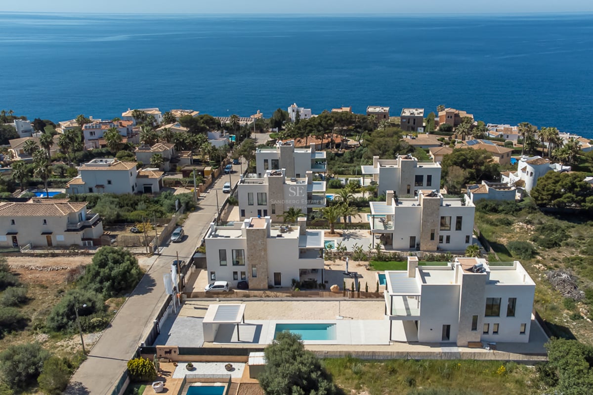 Vue aérienne d'un ensemble de villas blanches modernes avec piscines surplombant la mer Méditerranée.
