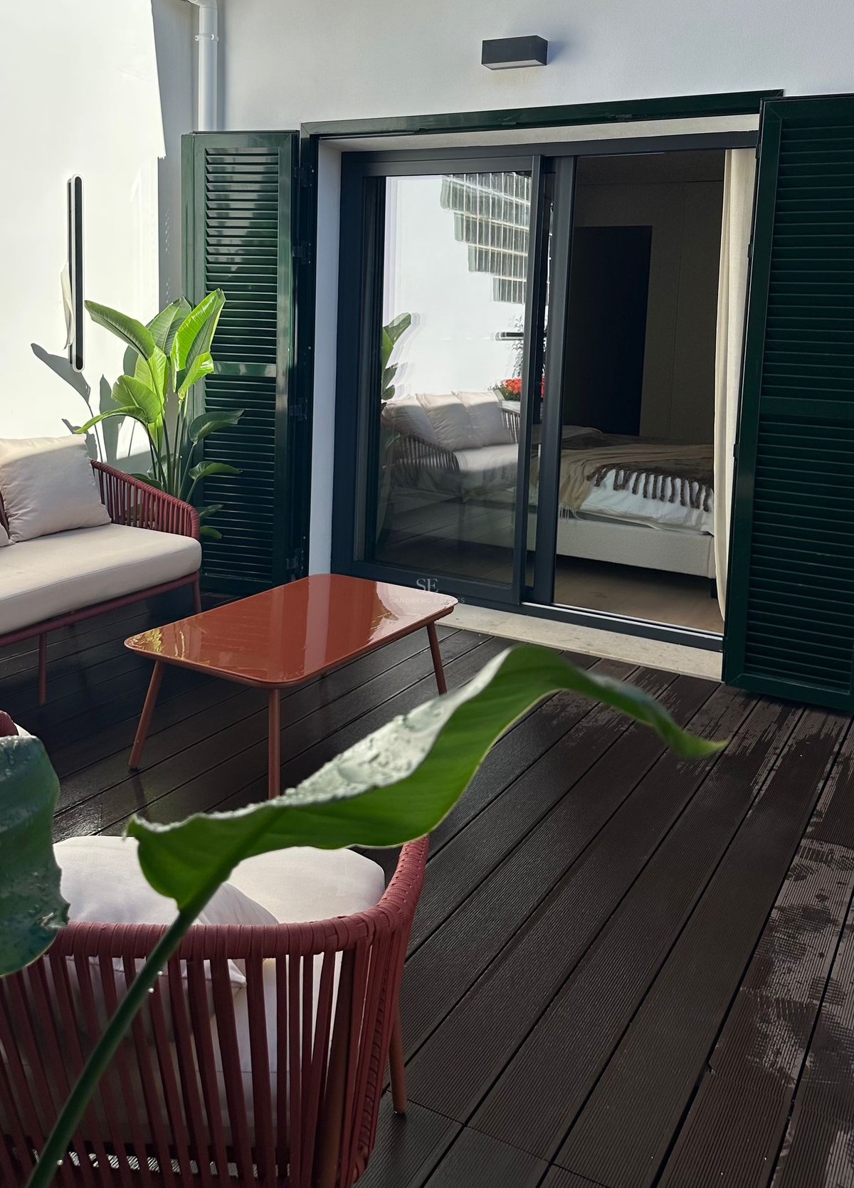 Terrasse privée avec mobilier terre cuite, plancher en bois et volets verts près de l'entrée de la chambre.