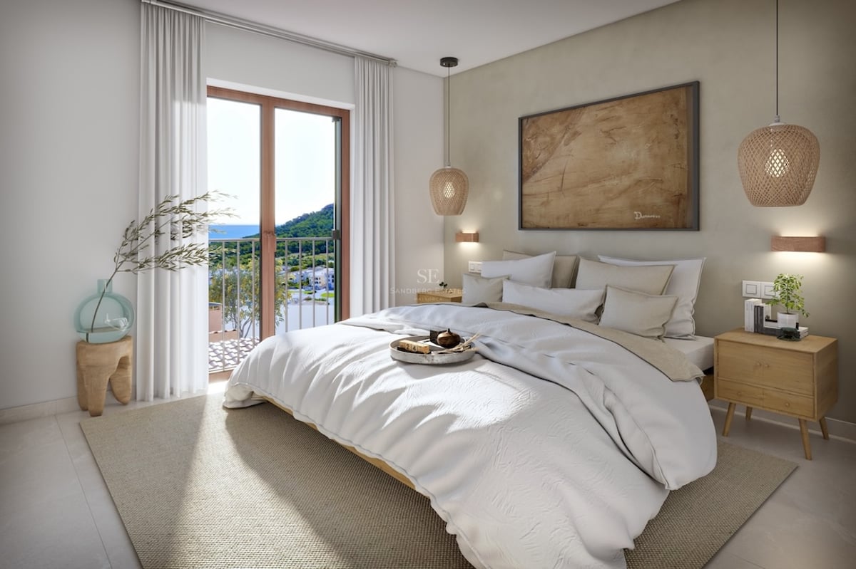 Bright modern bedroom with white bed, wicker lamps, wooden nightstands, and a balcony overlooking the sea and mountains.