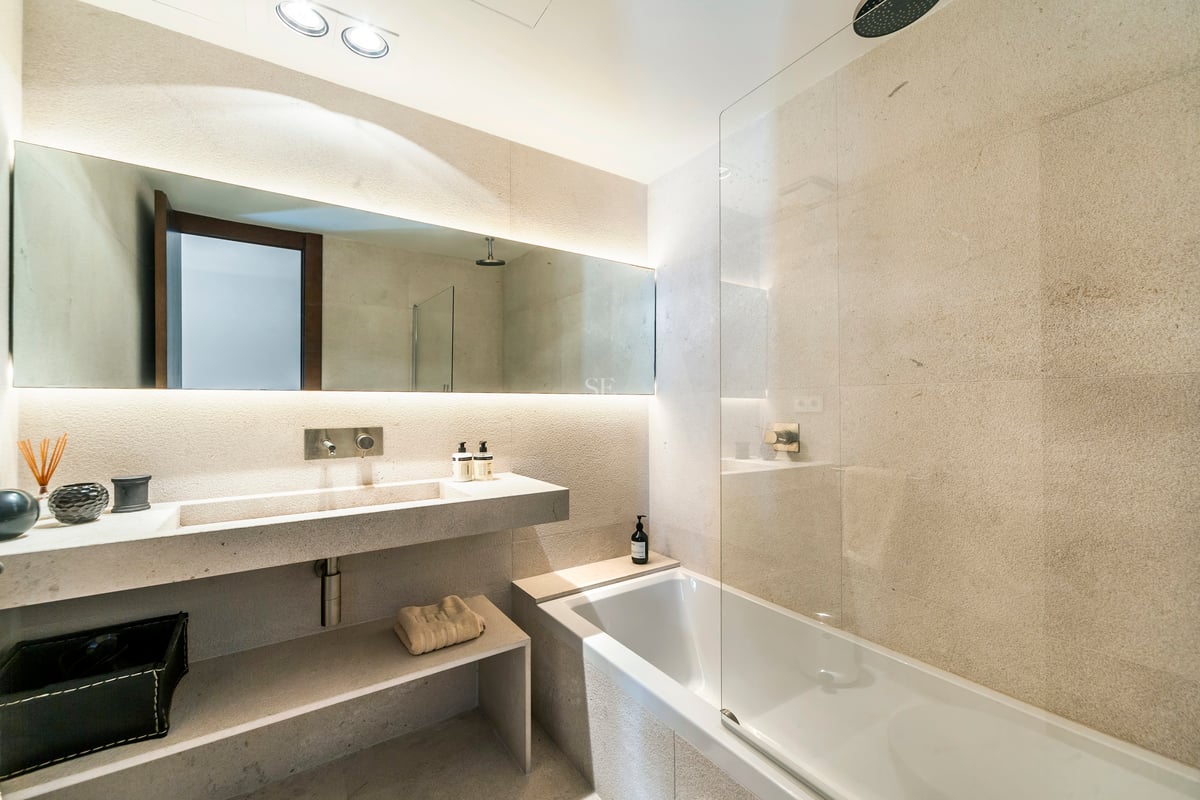 Salle de bains de luxe avec vasque en pierre, miroir rétroéclairé et baignoire avec paroi en verre.