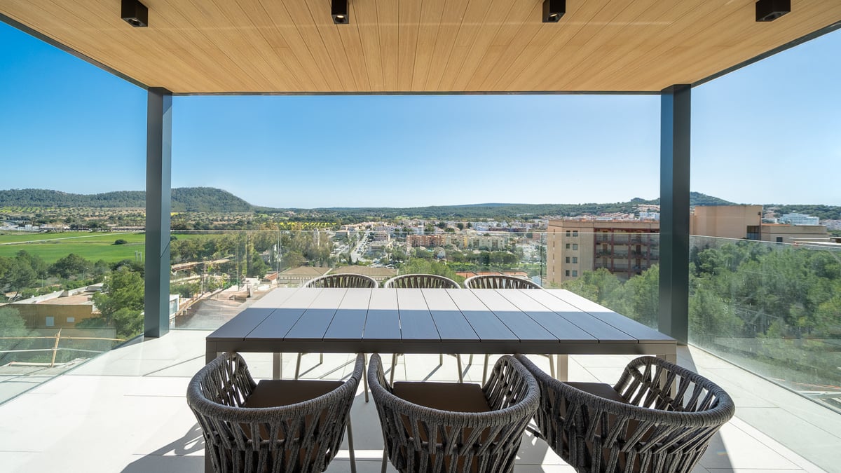 Terrasse couverte avec garde-corps en verre et table à manger pour six personnes surplombant une vallée et des collines.