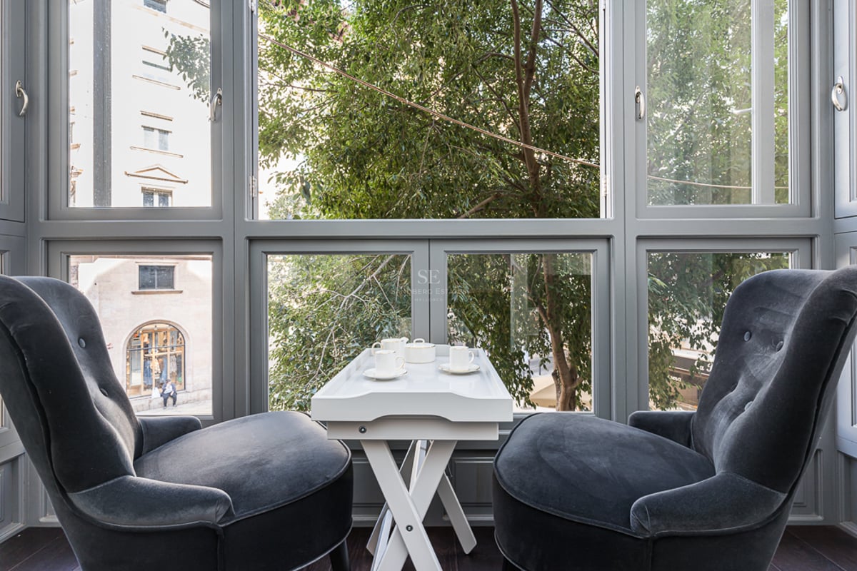 Deux fauteuils en velours gris devant une grande fenêtre avec une table à thé blanche et vue sur les arbres.