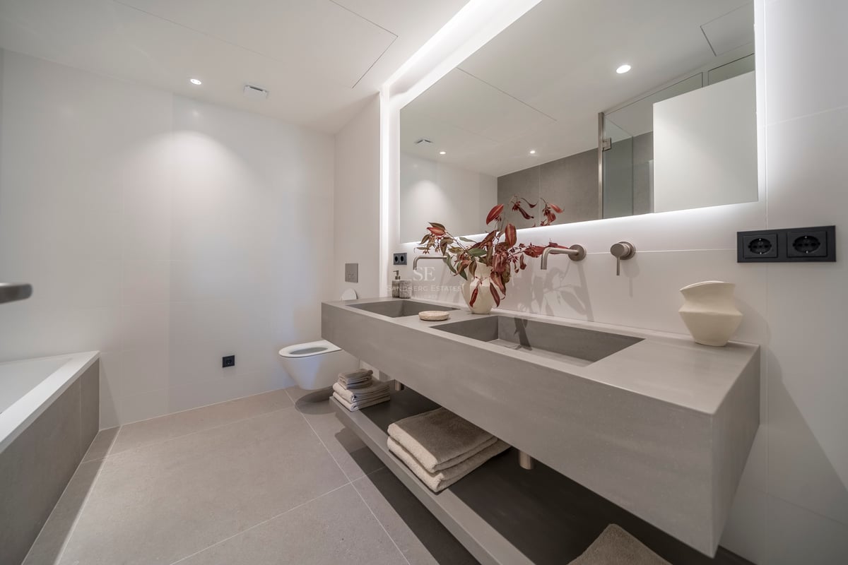 Salle de bain minimaliste avec double vasque flottante grise, grand miroir rétroéclairé et robinetterie murale.