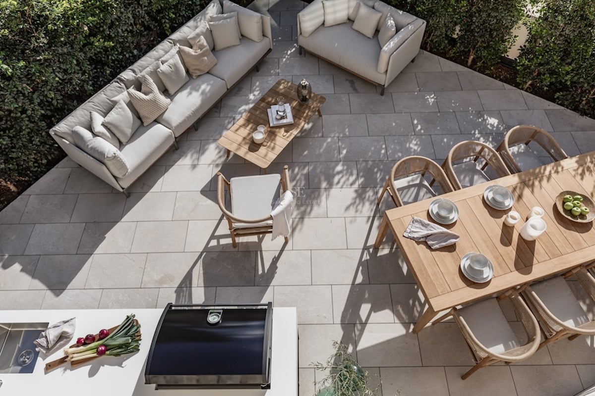 Vue plongeante sur une terrasse en pierre avec canapés design, table en bois et cuisine extérieure entourée de verdure.