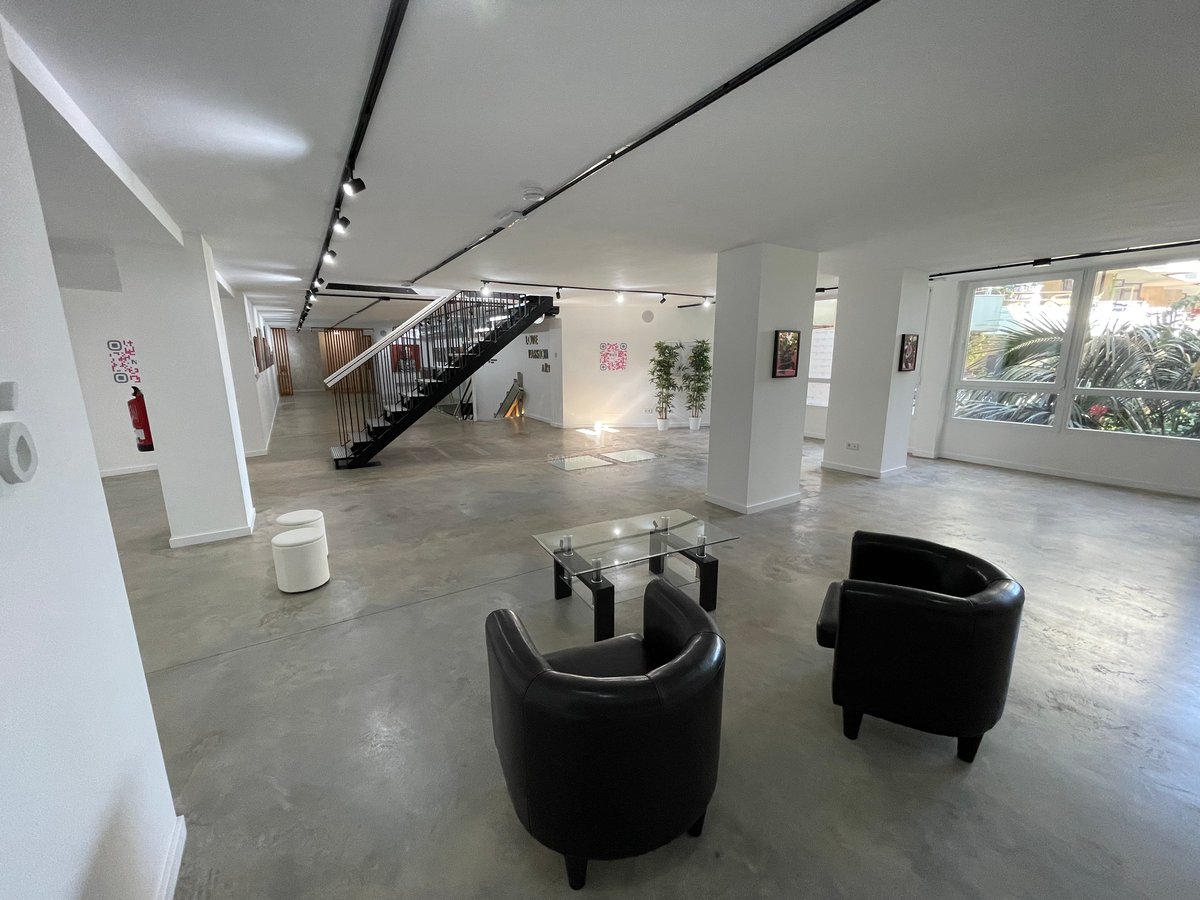 Espace vaste avec sols en béton poli, fauteuils en cuir noir et un escalier métallique minimaliste.