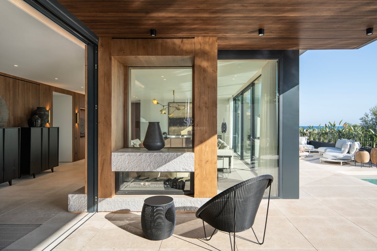 Terrasse contemporaine couverte avec cheminée en pierre double face, finitions en bois et vue sur la mer Méditerranée.