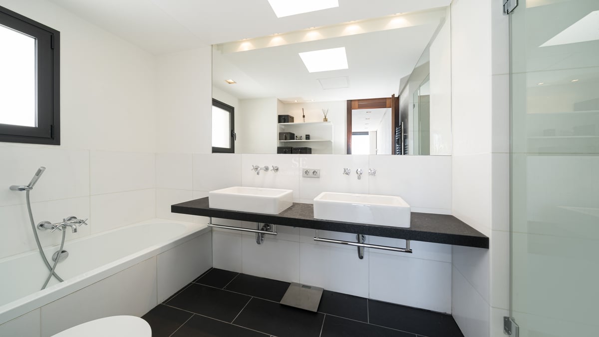 Salle de bain moderne et lumineuse avec double vasque suspendue noire, vasques blanches, grand miroir et douche vitrée.