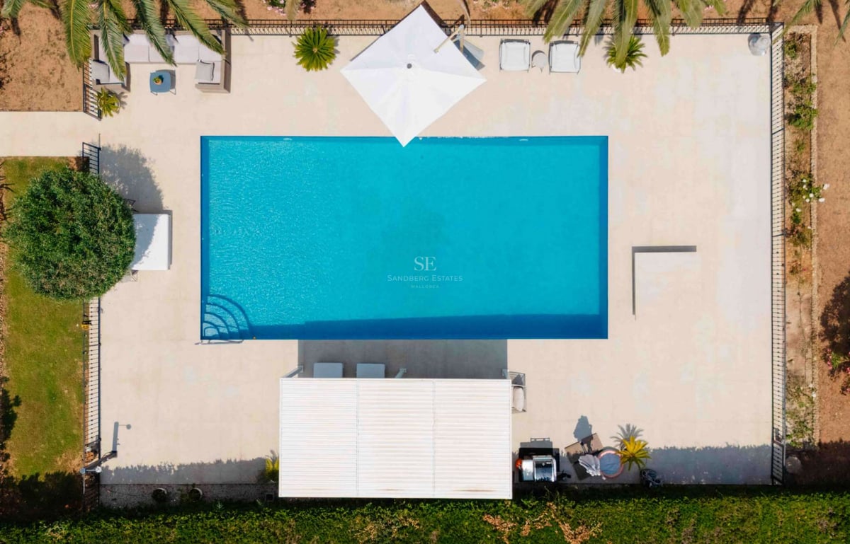 Vue aérienne d'une piscine rectangulaire turquoise entourée d'un dallage en pierre naturelle et de palmiers.