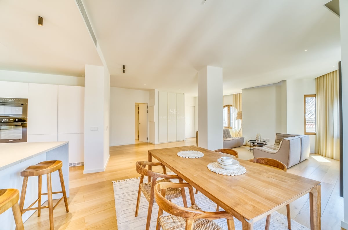 Bright open-plan living room featuring a light oak dining set, white minimalist kitchen, and floor-to-ceiling windows.