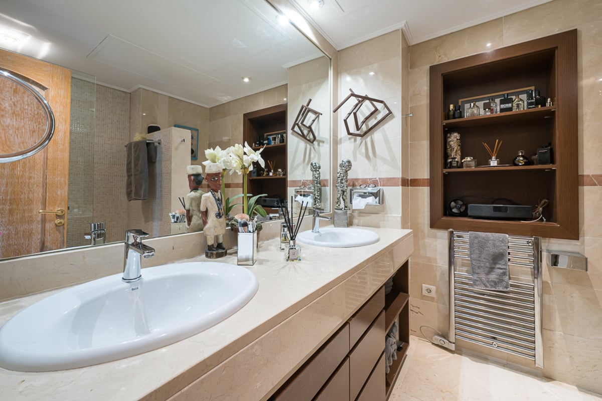 Salle de bains moderne avec deux vasques blanches, plan en marbre crème, grand miroir et étagères en bois encastrées.
