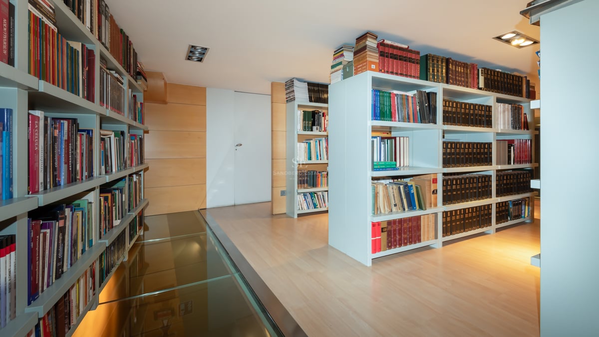 Modern home library with white floor-to-ceiling bookshelves and a transparent glass walkway over light wood flooring.