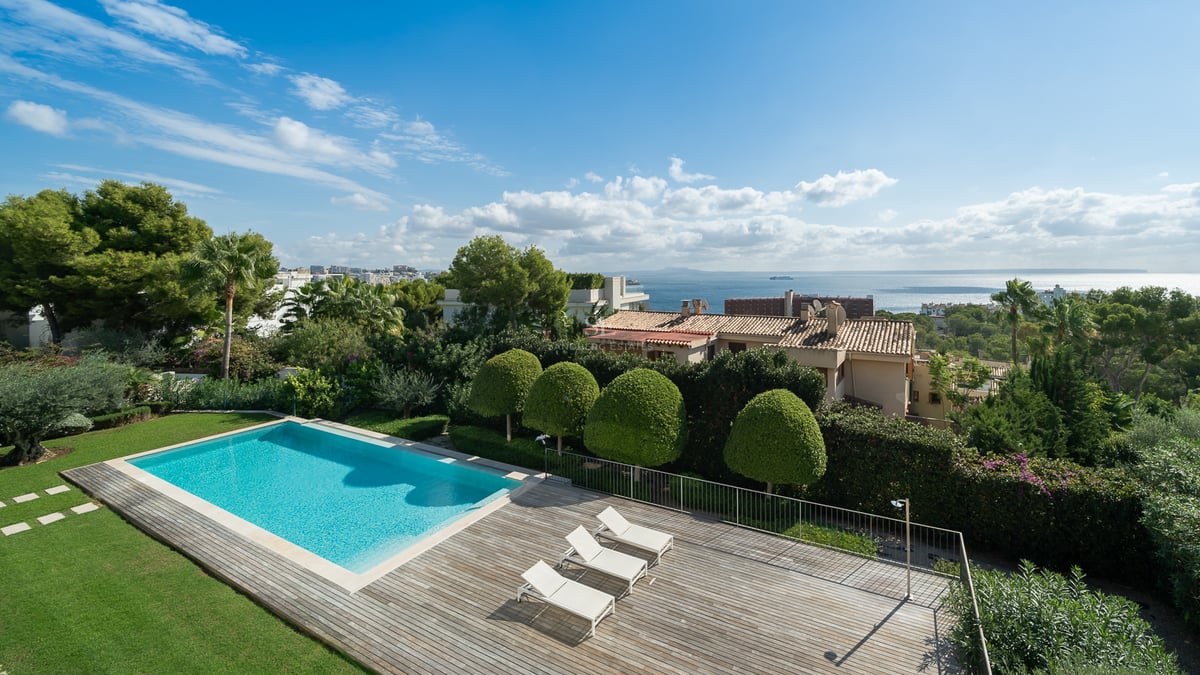 Vue en hauteur d'une piscine rectangulaire turquoise à côté d'une terrasse en bois avec des chaises longues blanches.