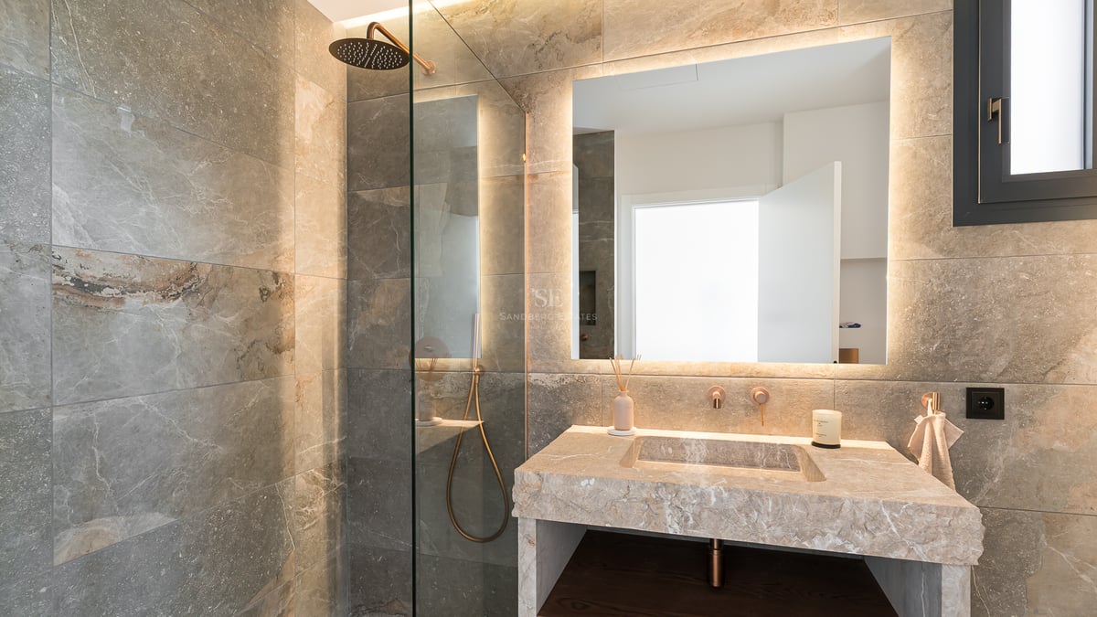 Salle de bains de luxe avec douche à l'italienne, vasque en pierre et grand miroir rétroéclairé avec lumière chaude.