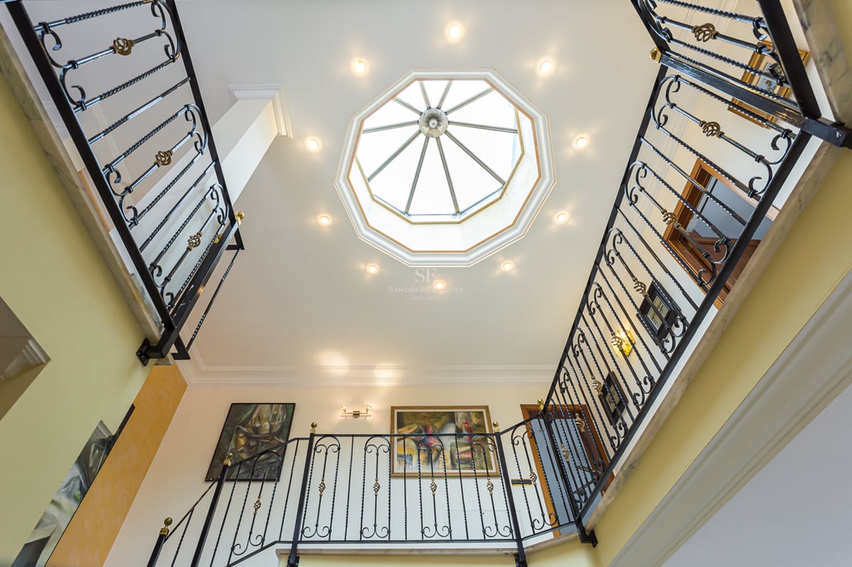 Vue vers le haut d'un grand escalier avec rampes en fer forgé et un puits de lumière octogonal au plafond.