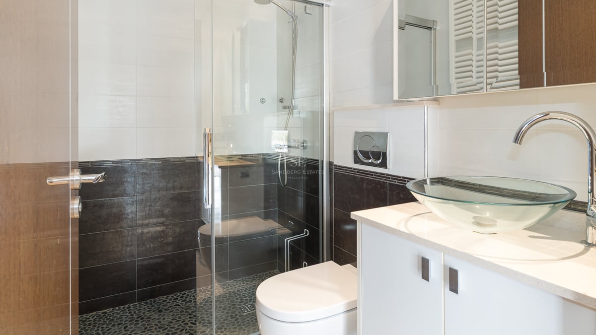 Salle de bain moderne avec vasque en verre, vanité blanche et douche vitrée avec sol en galets.