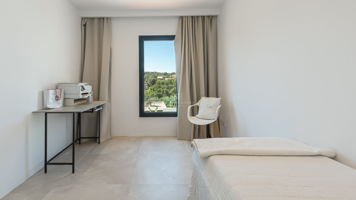Chambre lumineuse avec lit blanc, bureau minimaliste et fenêtre offrant une vue sur les collines.