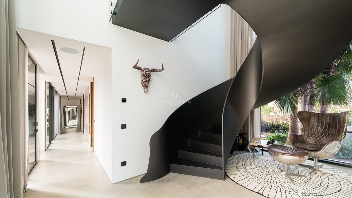 Escalier en colimaçon moderne en métal noir mat dans une villa lumineuse aux murs blancs.