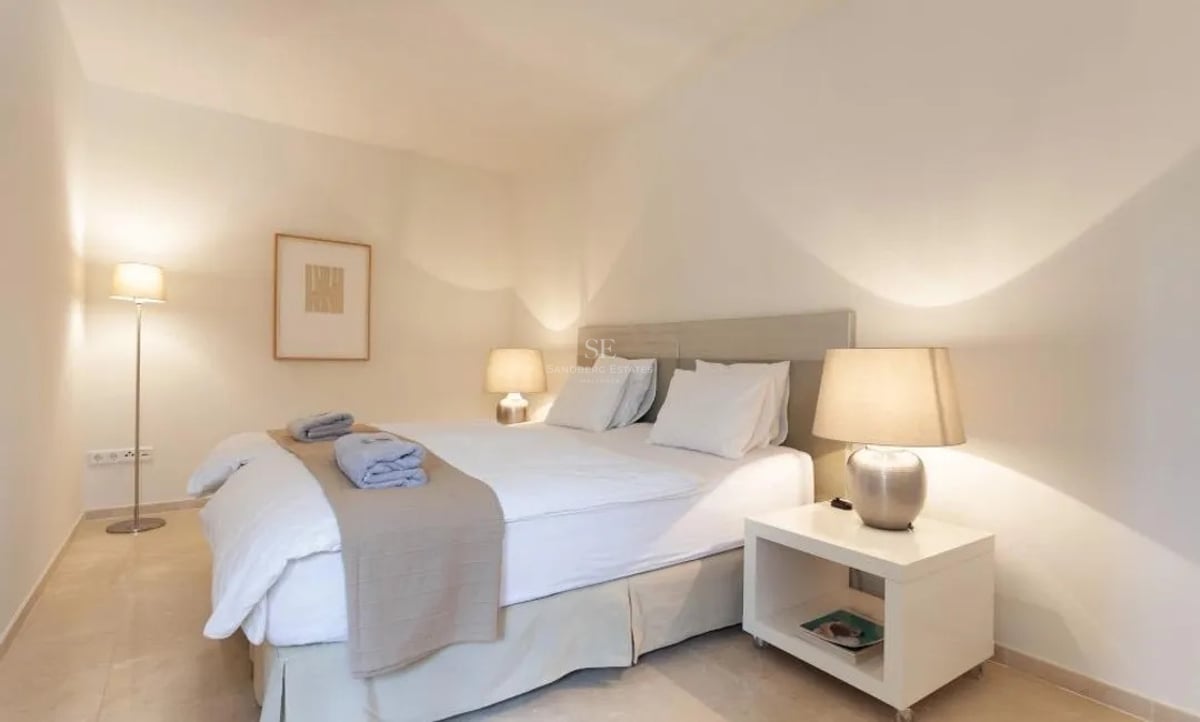 Chambre moderne avec lit double, draps blancs, lampes de chevet et sol en pierre naturelle.