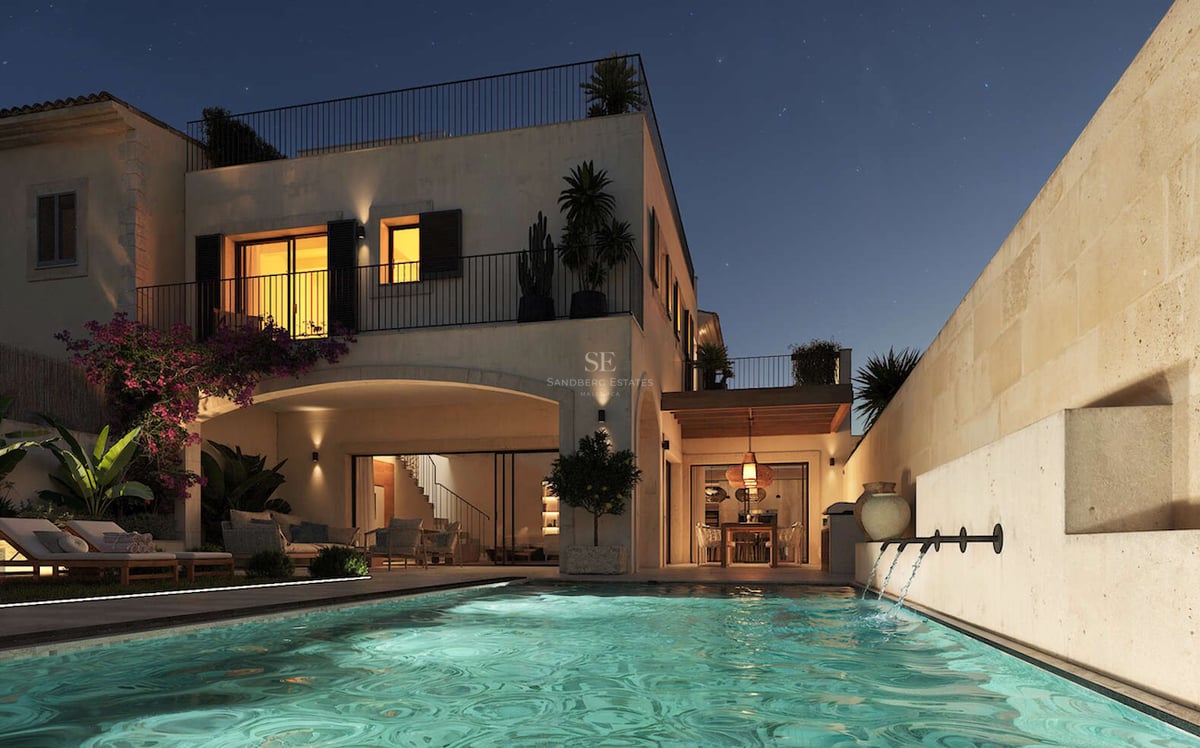 Vue nocturne d'une villa de luxe avec piscine éclairée, jets d'eau, murs en pierre et ciel étoilé.