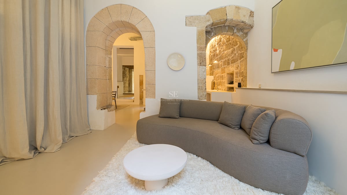 Un salon moderne avec un canapé gris incurvé, un tapis blanc et de grandes arches en pierre historiques.