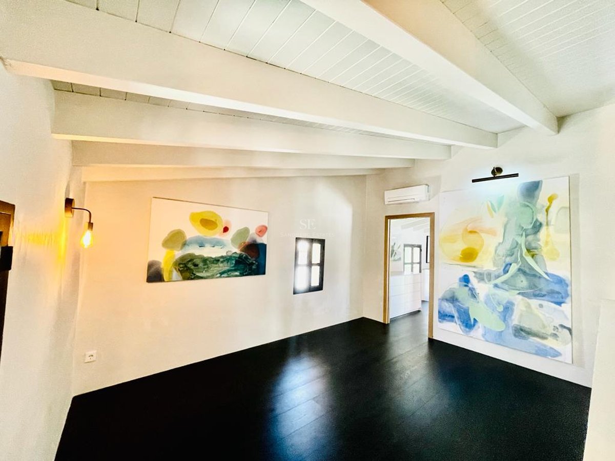 Pièce moderne avec plafond à poutres blanches, parquet sombre et grands tableaux abstraits sur murs blancs.
